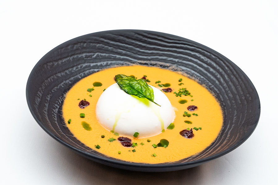 Burrata over tomato soup and basil with black olives
