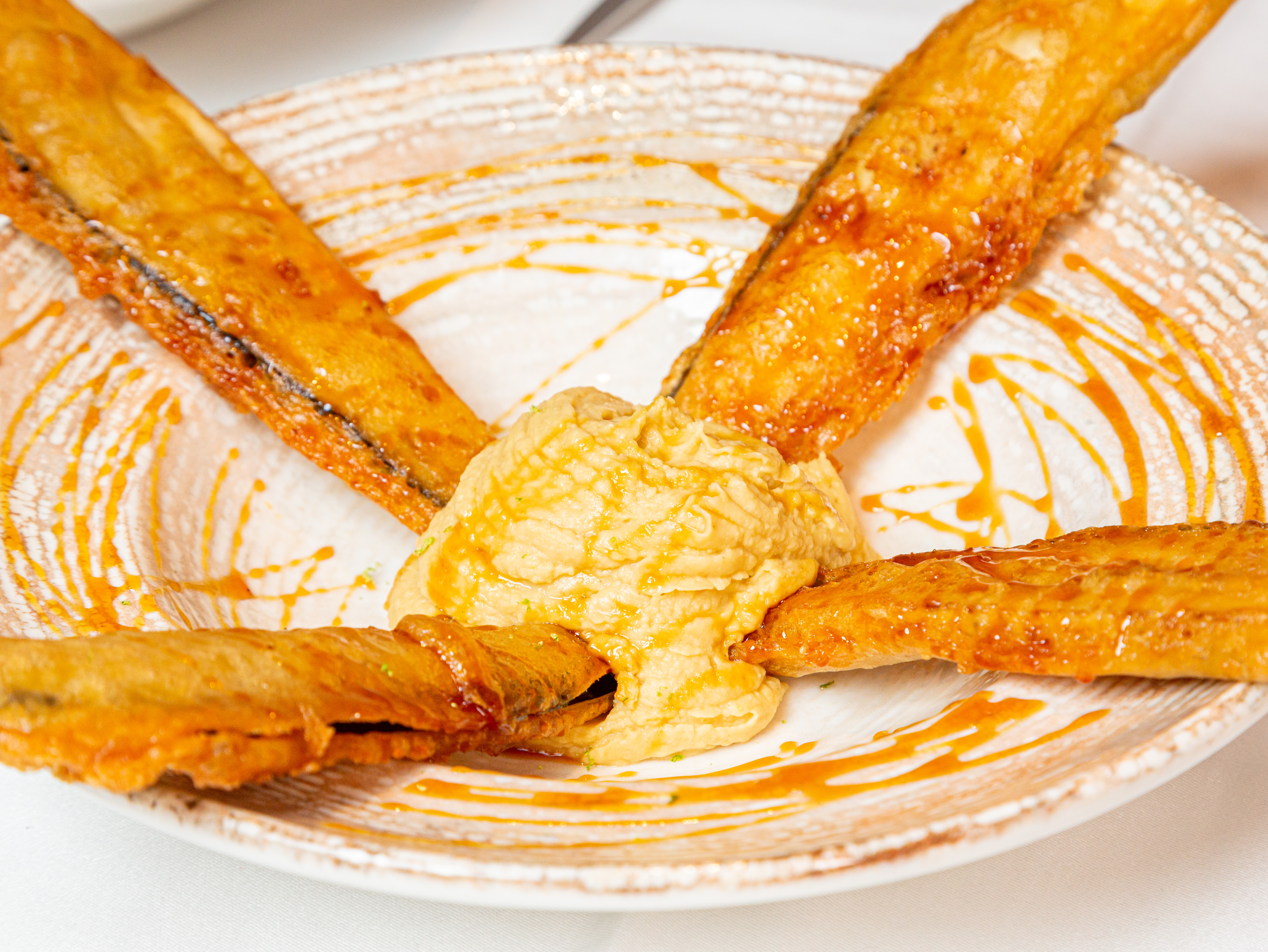Berenjenas en tempura sobre hummus cítrico y miel de caña