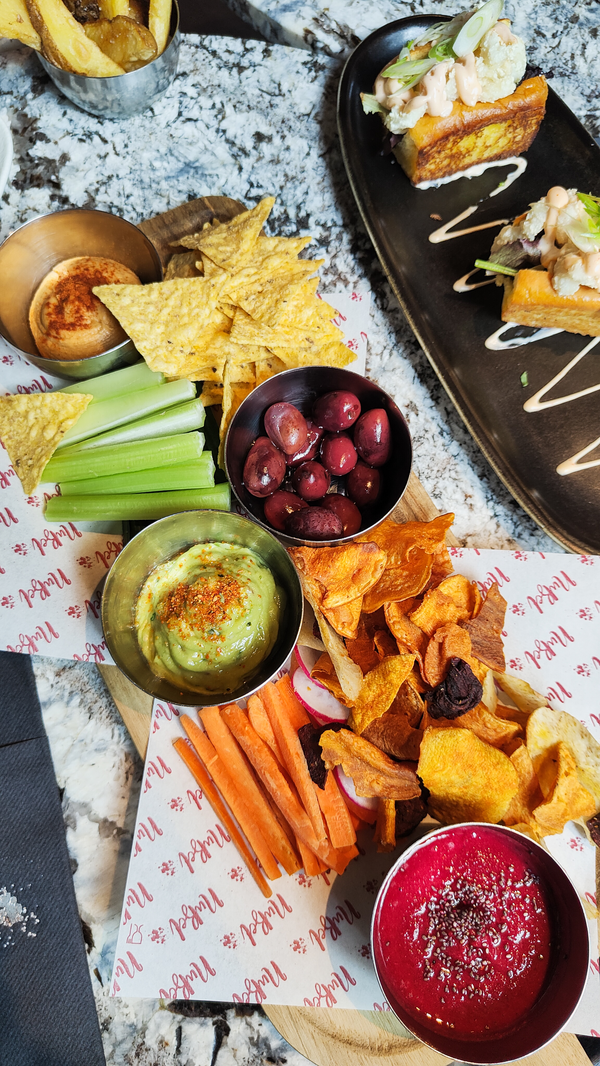 Table of guacamole, traditional hummus, beet hummus with tortilla chips, vegetable chips and veggie crudités.
